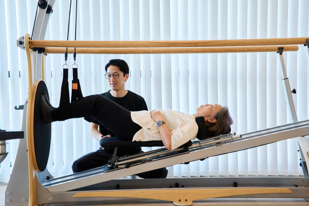 ジャイロトニックを用いた運動療法で、腰痛の再発予防トレーニングをする女性とサポートする理学療法士