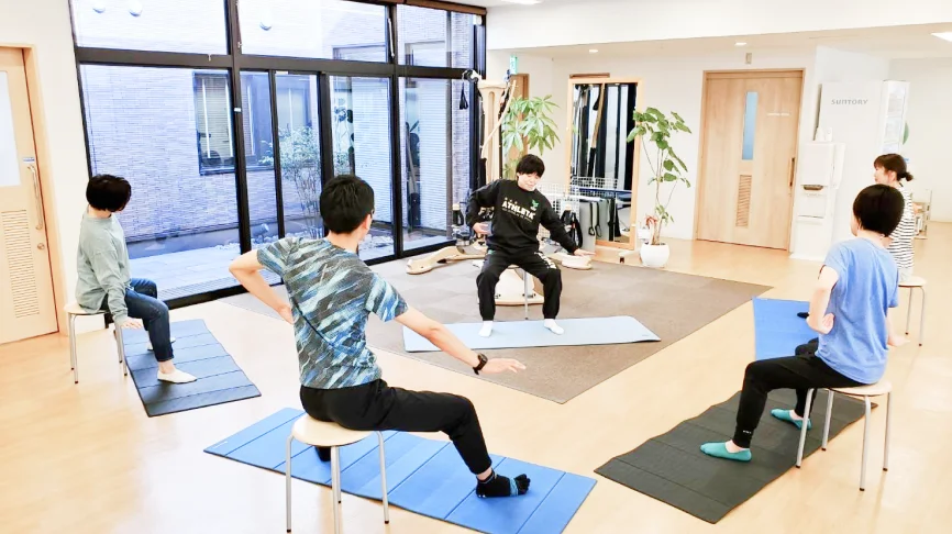 筋力バランスを改善トレーニングをする利用者と指導する理学療法士