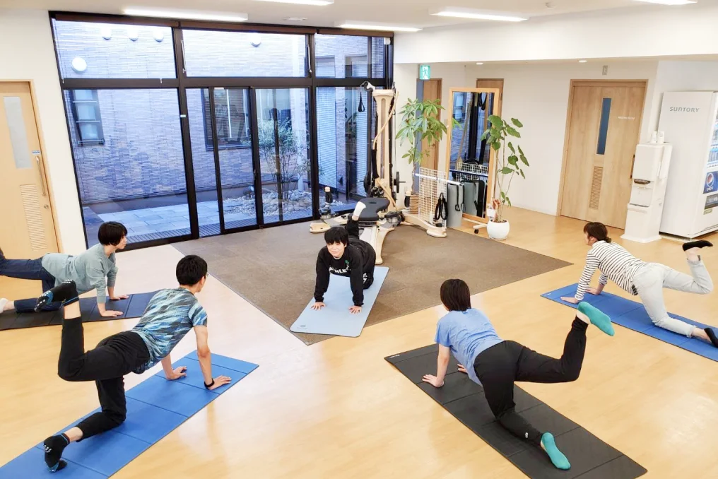 ジャイロキネシス®によるグループレッスンを受ける利用者と指導する理学療法士